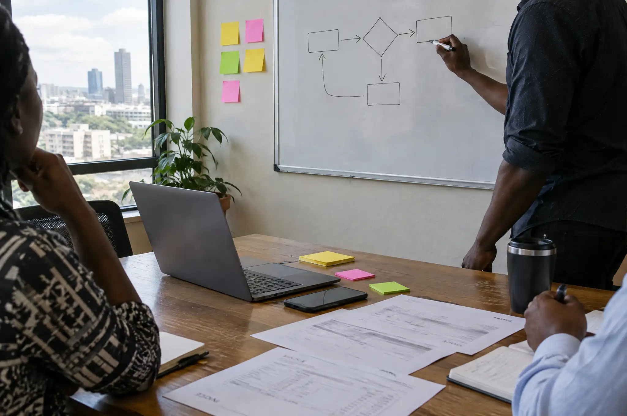 A working session: one person sketches a process flowchart on a whiteboard while others take notes at the table